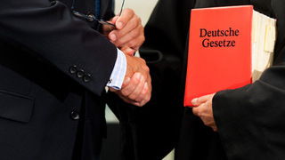 Foto: Zwei Personen geben sich die Hand / Ordner Deutsche Gesetze Foto: Zwei Personen geben sich die Hand / Ordner Deutsche Gesetze